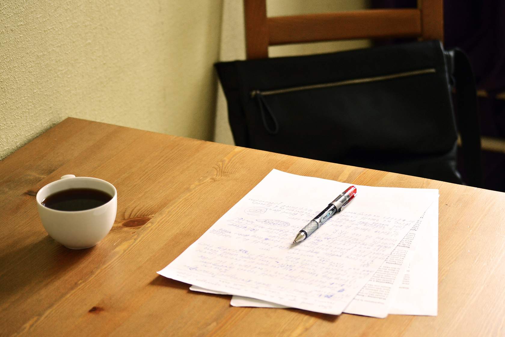 A table with paper, pen, and cup of coffee on it