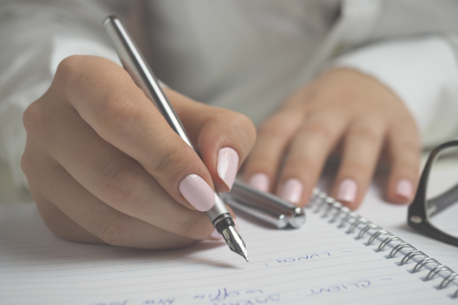 close up of person with rose pink nail polish, writing in a notebook
