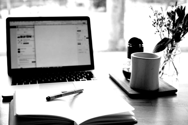open laptop, open book, pen, and coffee mug all on a desk