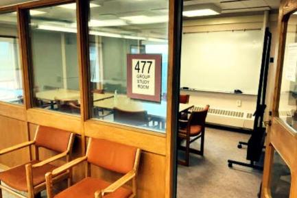An open door of a library group study room with tables, chairs, and a whiteboard.