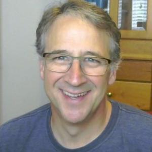 Curt wears glasses and is smiling while facing the camera. He has short brown hair with very small patches of distinguished gray hair on the sides.