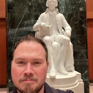 Casey standing in front of a statue of James Madison at the Library of Congress