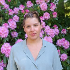 Gabriela standing in front of a rhododendron in bloom, wearing a green button-up blouse