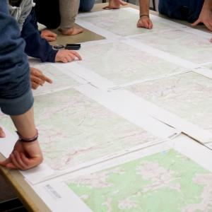 large table with maps spread out and people leaning over the maps