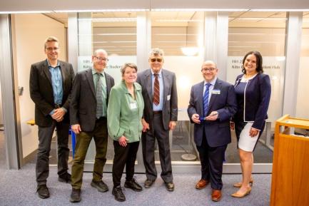 A group of people standing in front of the blue ribbon tied between the glass consultation rooms of the new Hub, moments before the ceremonial ribbon cutting. From left to right: Brad Johnson, David Patrick, Kathy Kitto, Dennis Waller, John Danneker, and Kim O’Neill.